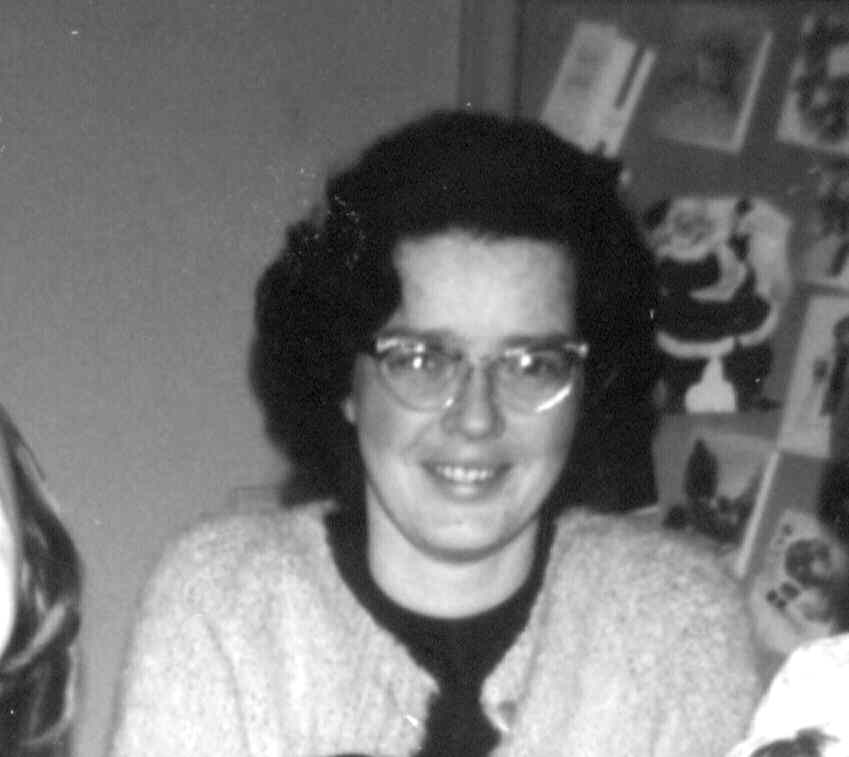 Judy Taylor as a young women with thick, wavy black hair, a light coloured cardigan. And clear glasses. Black and white photo.