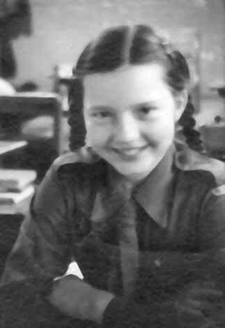 Judy Taylor as a child. Black and white photo. Smiling in a school classroom from the 1940s.