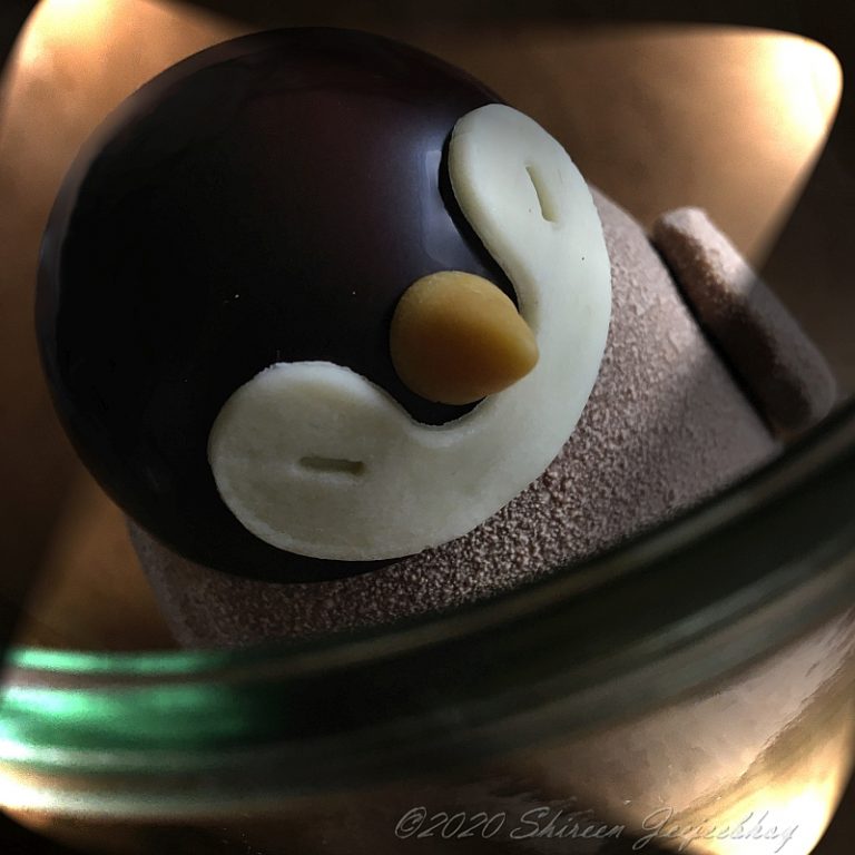 Chocolate penguin, top down view, with four lights highting its face of dark and white chocolate and part of the rim of the glass jar its in. Slanted overhead view.