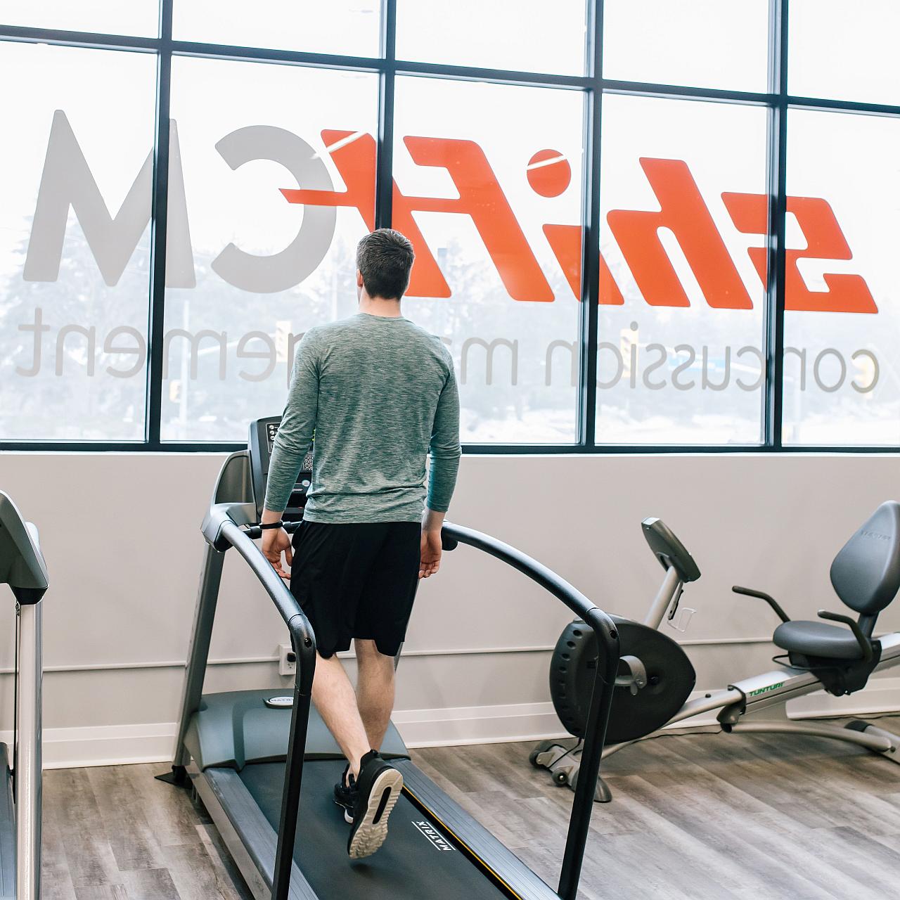 Man walking on a treadmill looking out the window with the name Shift Concussion Management across the outside of the window.