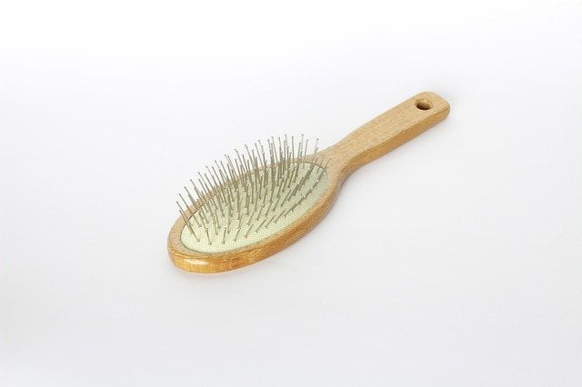 Hair brush made of blonde wood lying metal bristles up against a gradient white background.
