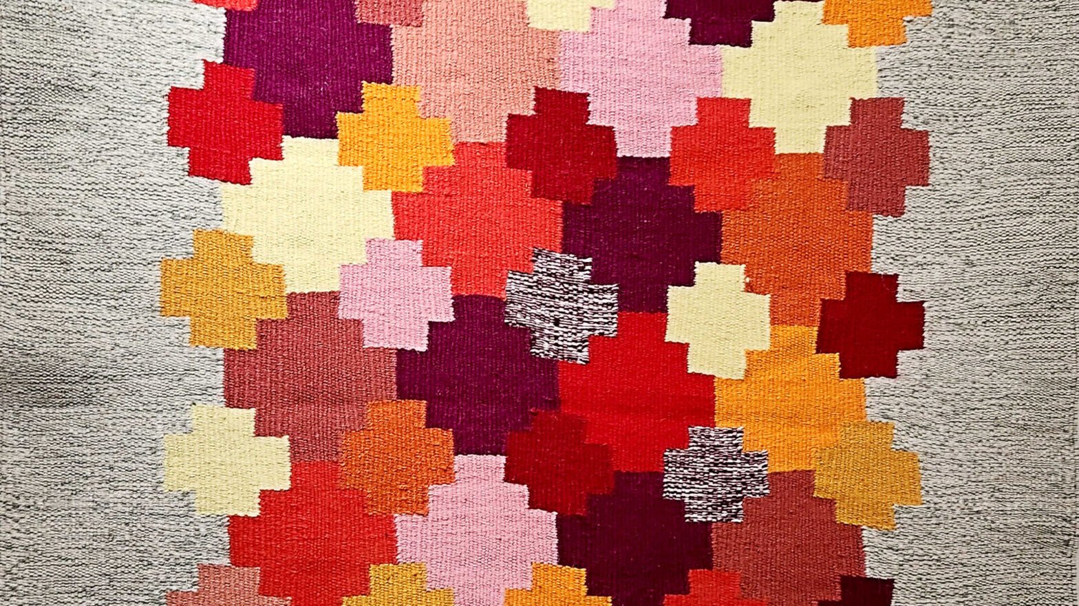 Square crosses of colour bordered by greys, woven into a tapestry.